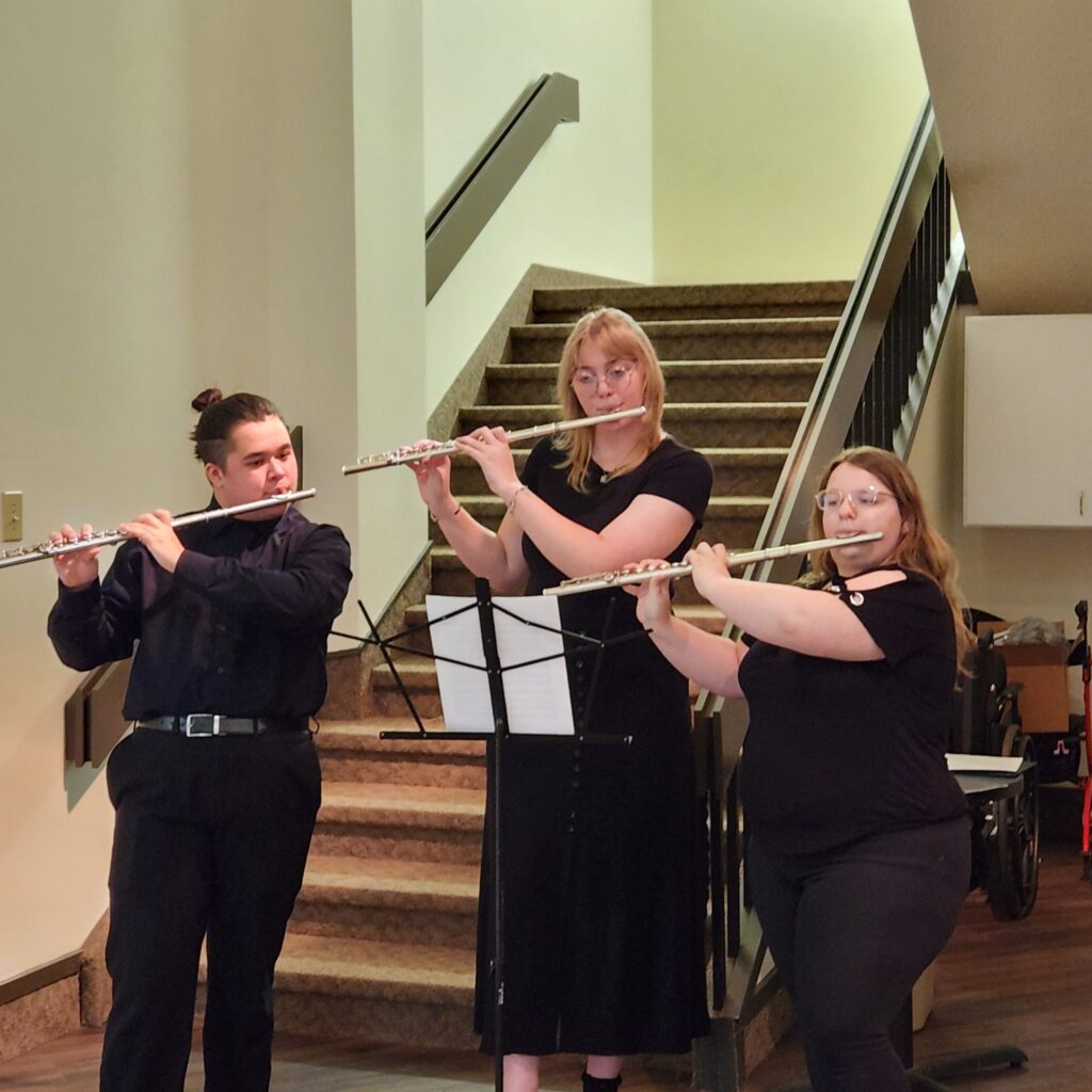 Three musicians playing flutes on a staircase indoors.