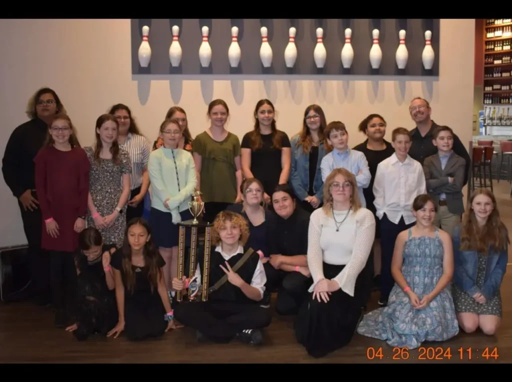 Group photo of diverse people posing indoors with bowling pins in the background.