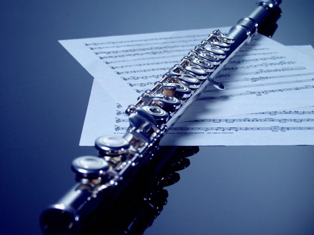 A silver flute resting on sheet music under soft lighting.