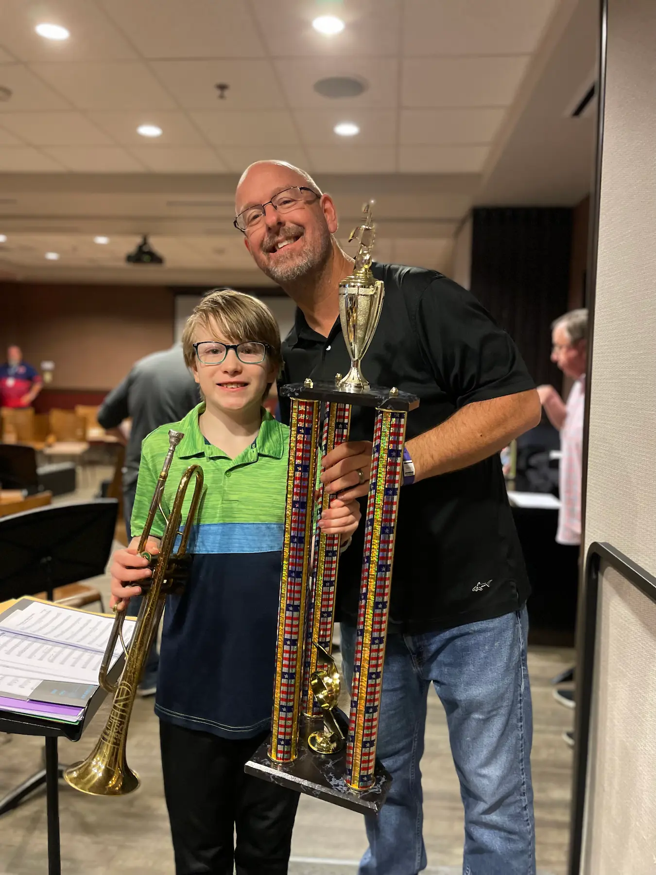 A man and a boy proudly hold a large trophy in a celebratory setting.